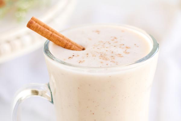 a frothy glass of eggnog with a cinnamon stick on top