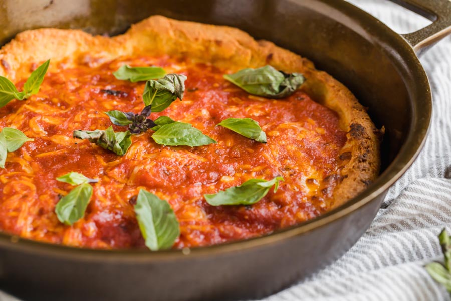 basil leaves scattered over a small pizza in a skillet