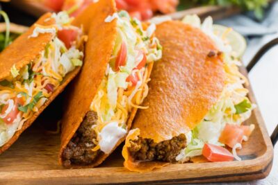 cheesy Doritos locos on a wood tray filled with ground beef, lettuce, cheese and sour cream