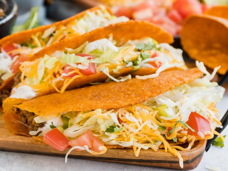 shredded cheese spilling out of three tacos lined up