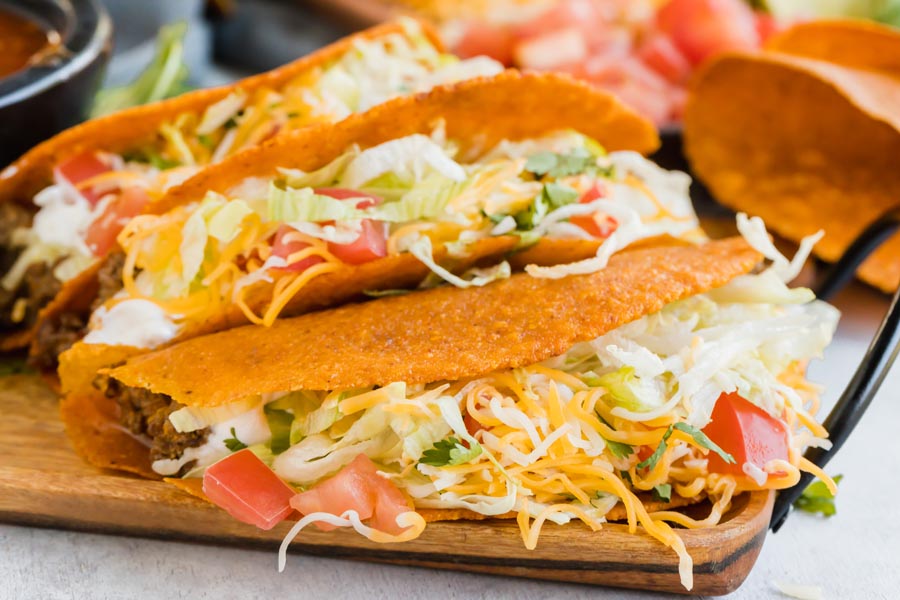 shredded cheese spilling out of three tacos lined up