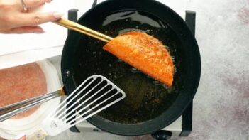 a doritos taco fries in a skillet in oil while a hand uses a spatula to hold the taco shell open