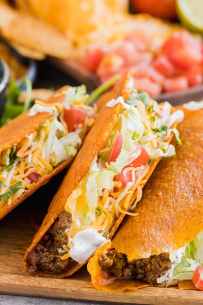 keto tacos filled with ground beef, sour cream, cheese, tomato and lettuce lined up in a row