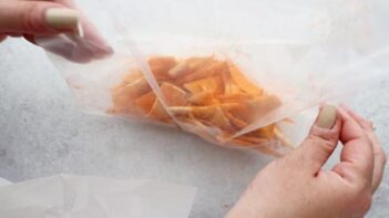 coating nacho cheese flavoring onto tortilla chips in a ziploc bag