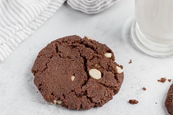 a chocolate cookies with white chips next to a striped towel and glass of milk