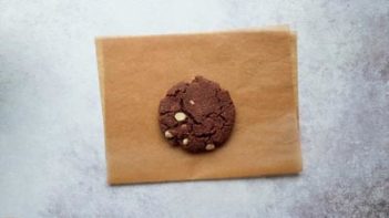a baked chocolate cookie with white chocolate chips on a half sheet of parchment paper