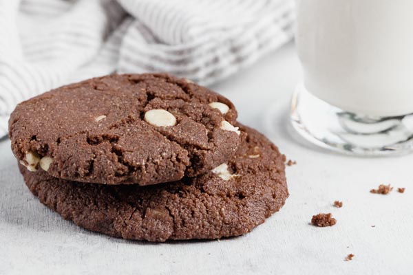 two chocolate cookies stacked on each other with crumbs and a glass of milk near by