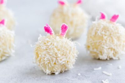 a coconut covered cheesecake bite that looks like an easter bunny with pink marshmallow ears