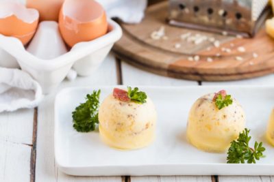 a row of egg bites on a white plate topped with parsley and crumbed bacon