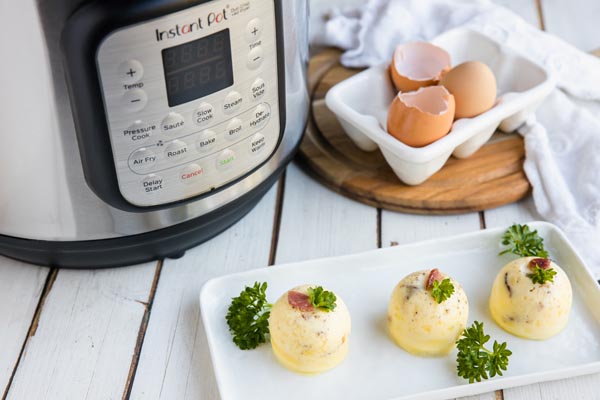 egg bites on a white plate in front of a pressure cooker next to a carton of eggs