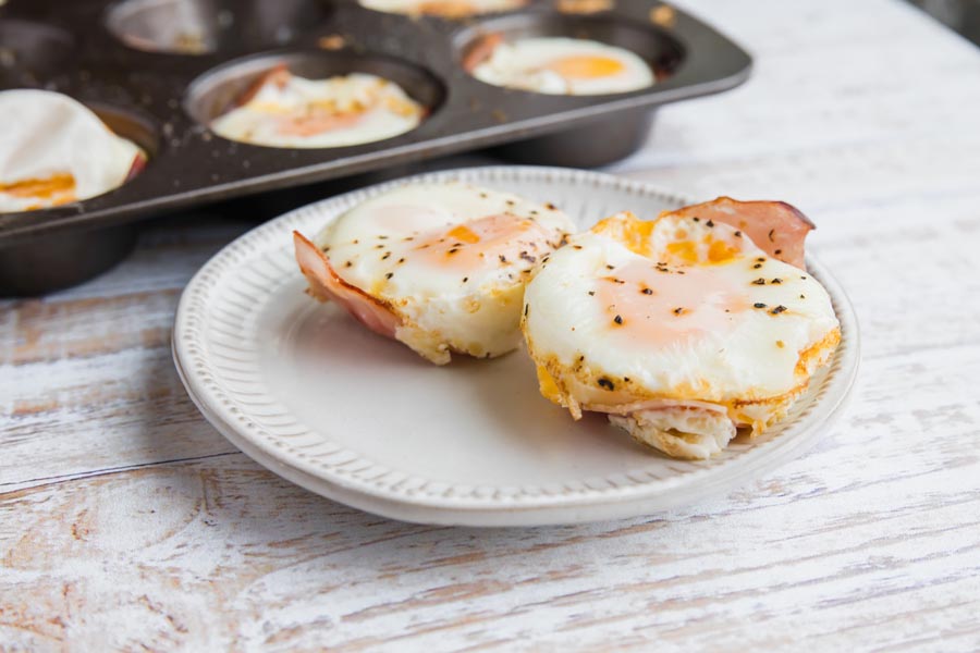 two ham egg cups on a plate with a muffin tray in the background