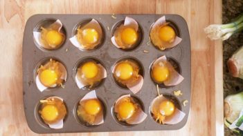 raw egg cracked in a muffin pan with a slice of ham underneath