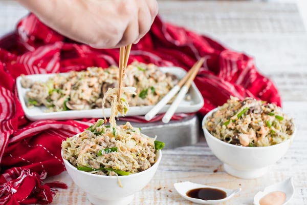 using wooden chopsticks to put up a bite of cabbage egg roll stir fry from a white bowl with a red scarf in the background along with two other bowls of egg roll mixture
