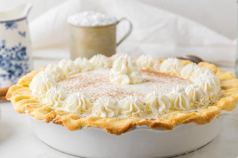 A side view of the whole keto eggnog pie in a pie dish topped with whipped cream rosettes and nutmeg.