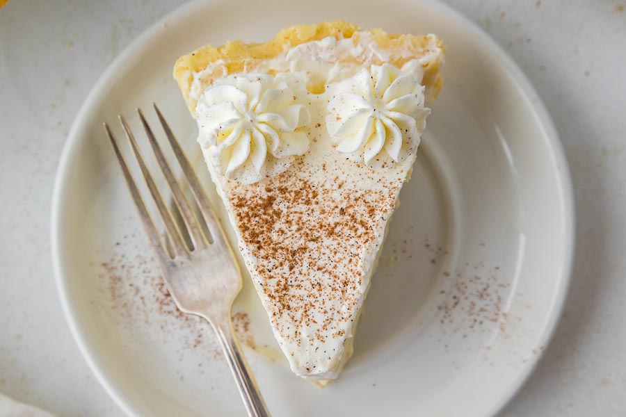 A single slice of keto eggnog pie on a plate with two piped whipped cream dollops and nutmeg sprinkled on top.