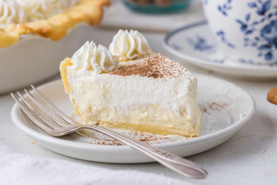 A plated slice of keto eggnog pie showing creamy layers and a buttery crust with a fork beside it.