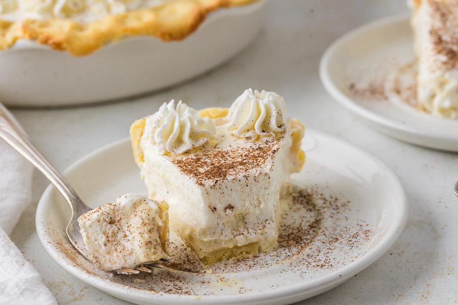 A bite taken from a slice of keto eggnog pie on a plate with whipped cream and nutmeg scattered around.