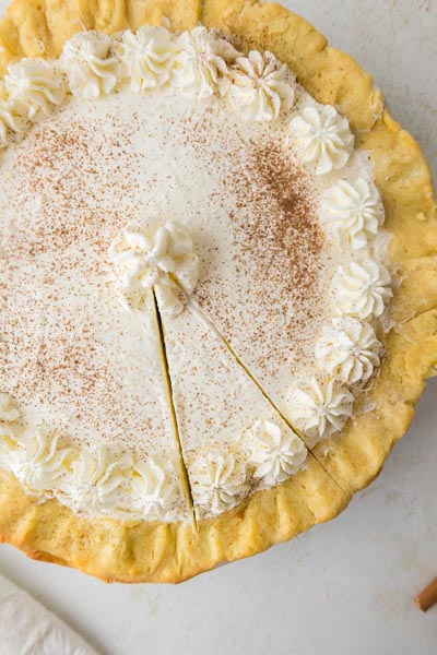 An overhead view of the keto eggnog pie topped with whipped cream and a generous dusting of nutmeg with one slice removed.