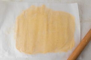 Pie dough rolled flat between two sheets of parchment paper with a rolling pin.