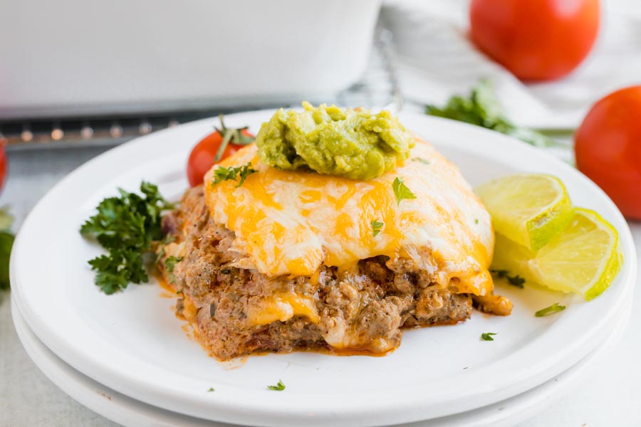 a portion of enchilada casserole on a white plate with tomato and guac on top