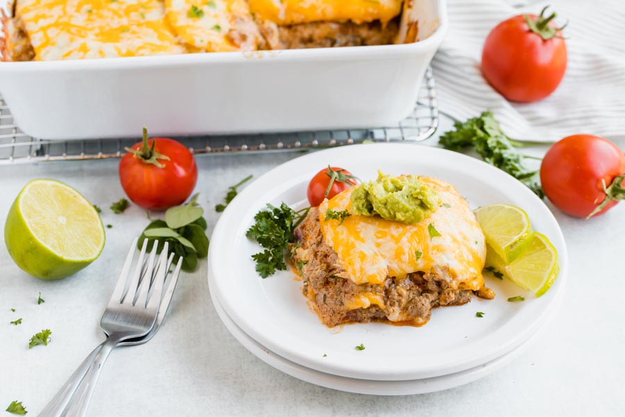 a slice of enchilada lasagna casserole in front of a casserole dish