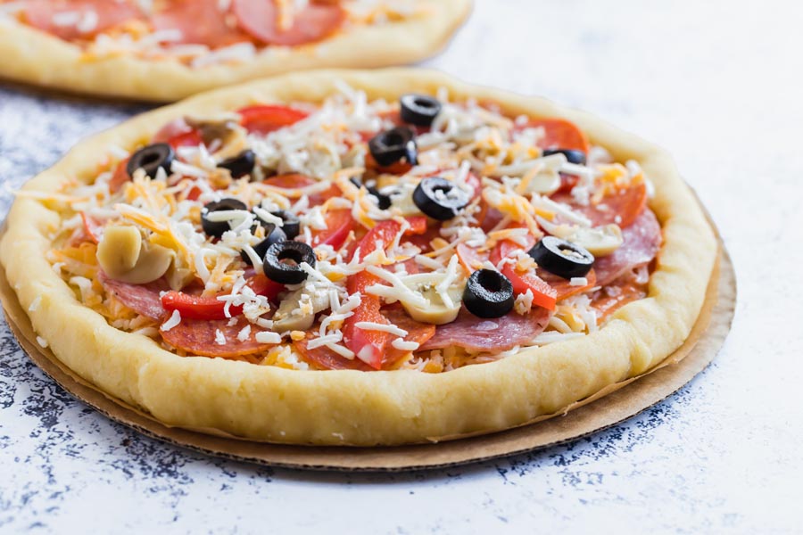 an unbaked combination pizza with olives, mushrooms, pepperoni and salami