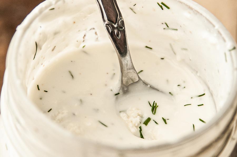 a spoon with white salad dressing on it inside the jar