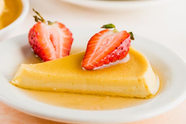 a slice of flan on a plate topped with sliced strawberries