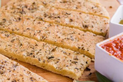 Focaccia flatbread covered with Italian seasoning sliced into strips next to marinara sauce.