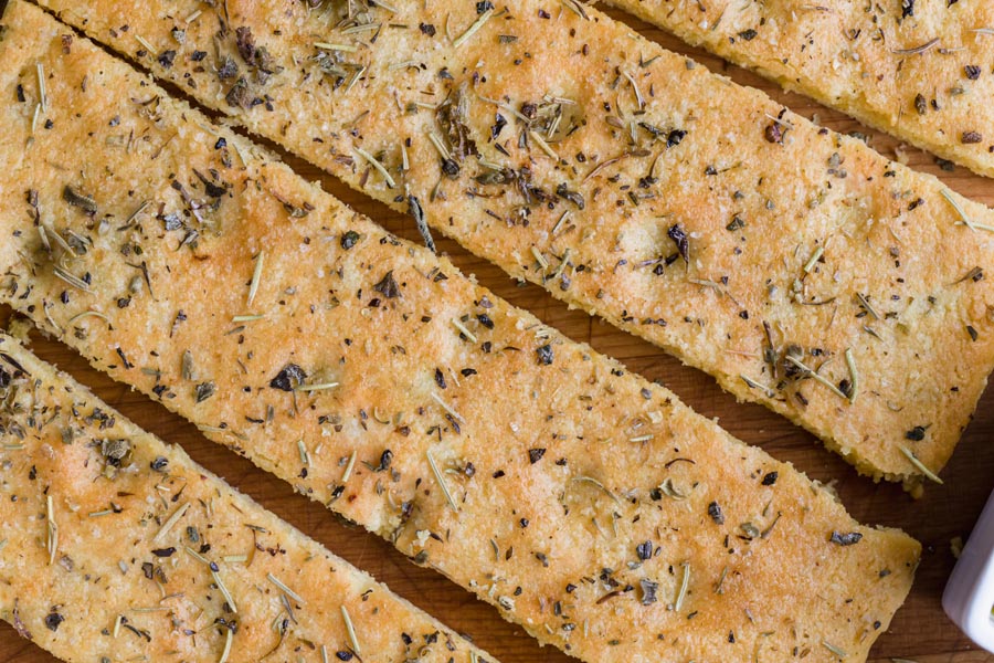 Crispy focaccia topped with herbs and oil with dimples on the top.