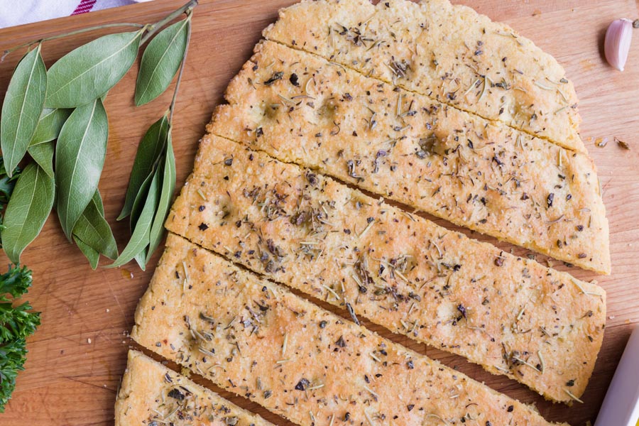 Dimpled focaccia bread cut into strips next to bay leaves and garlic cloves.