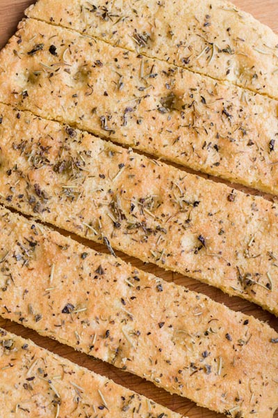 Close up of the dimples of focaccia bread cut into pieces and topped with herbs.