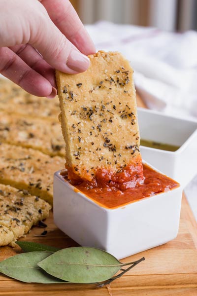 Hand dipping a piece of focaccia into red marinara sauce.