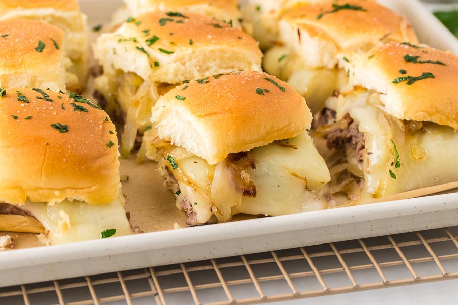 A tray of baked keto French dip sliders with golden rolls, melty cheese, and shaved beef tucked inside.