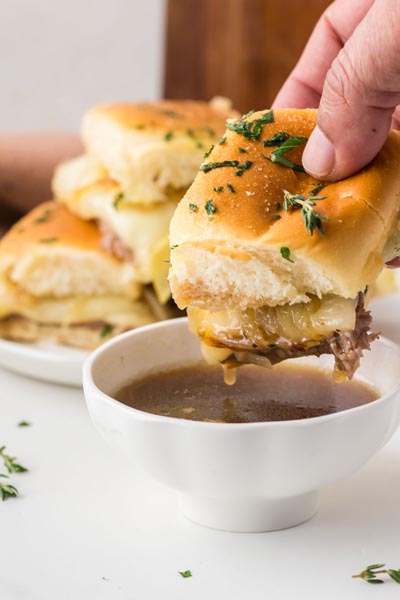 A hand dipping a keto French dip slider into a bowl of rich au jus gravy.