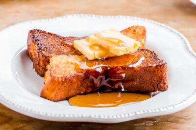 Close-up of syrup dripping down from a thick slice of french toast.