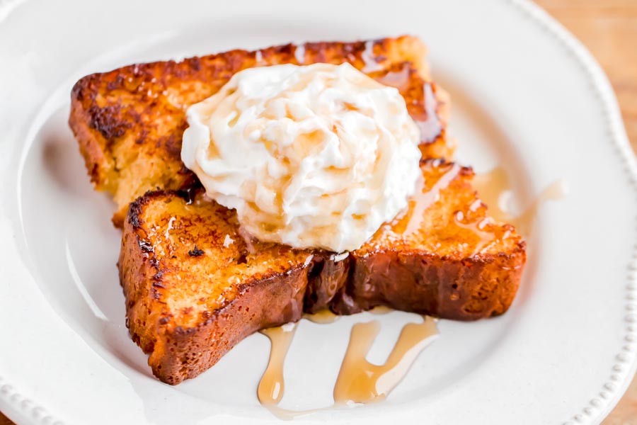 Close up of syrup drizzled over fried french toast that is topped with whipped cream.