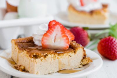 syrup dripping from a breaded casserole with strawberry slices and whipped cream on top