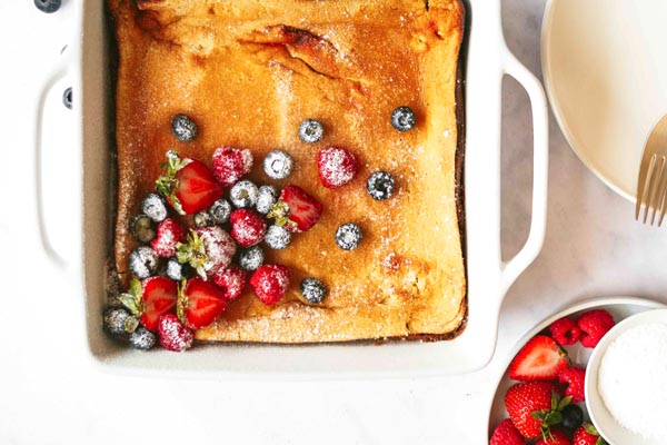 baked french toast casserole topped with berries and sugar free powdered sweetener in a casserole dish