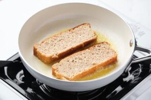 Two slices of french toast frying in a white skillet.