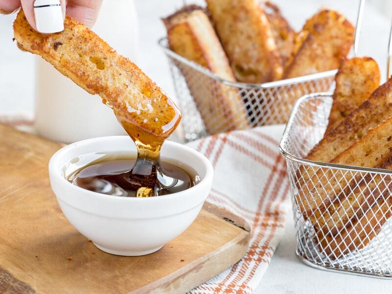 dipping a french toast stick into a bowl of maple syrup