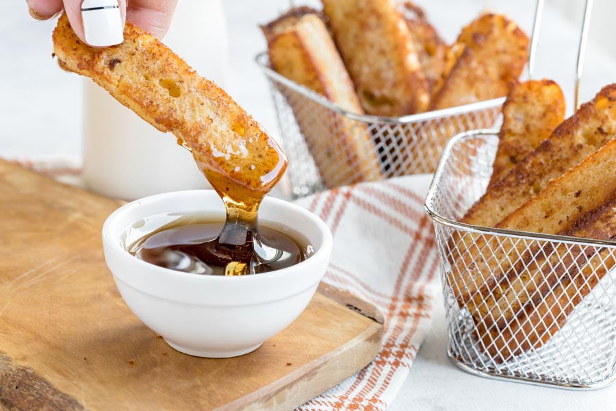 dipping a french toast stick into a bowl of maple syrup