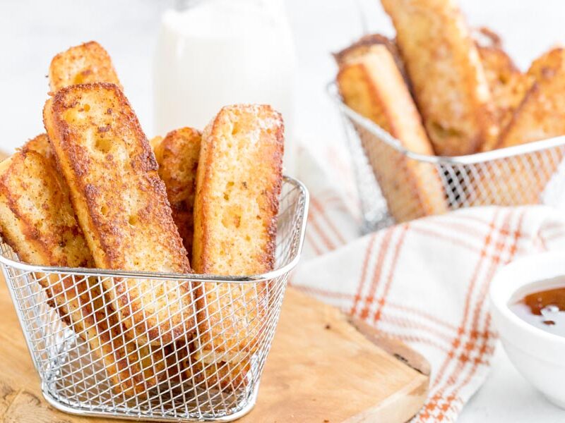 two small baskets with french toast pieces inside and a bowl of syrup nearby