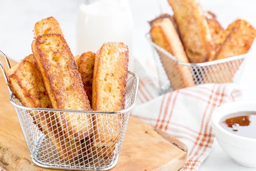 two small baskets with french toast pieces inside and a bowl of syrup nearby