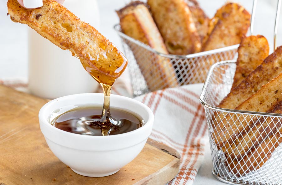 syrup dripping from a fried french toast stick hanging over a bowl of syrup