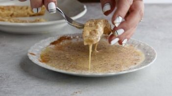 lifting a slice of bread out of the egg mixture with a fork while egg drips down