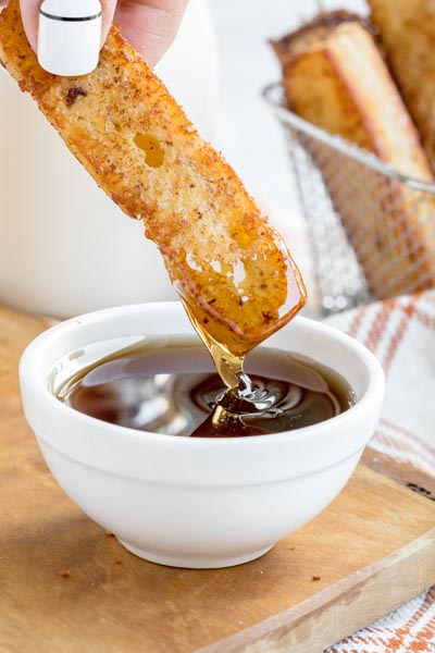 dunking a fried french toast stick in a bowl of syrup