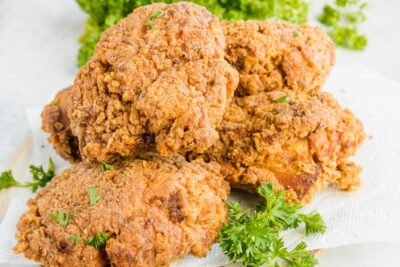 A pile of crispy fried chicken on a paper towel with sprigs of parsley nearby.