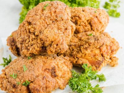 A pile of crispy fried chicken on a paper towel with sprigs of parsley nearby.