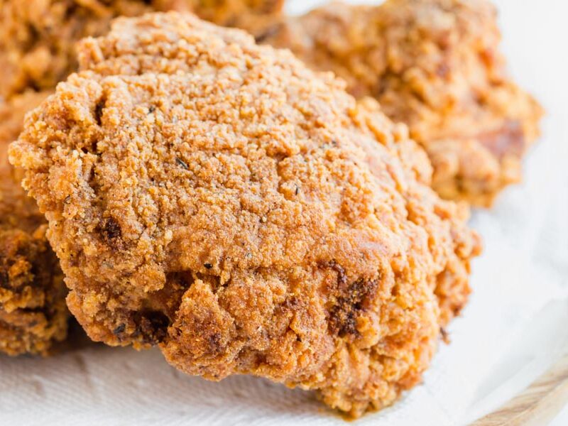 Close up of crunchy fried piece of chicken on a paper towel lined plate.